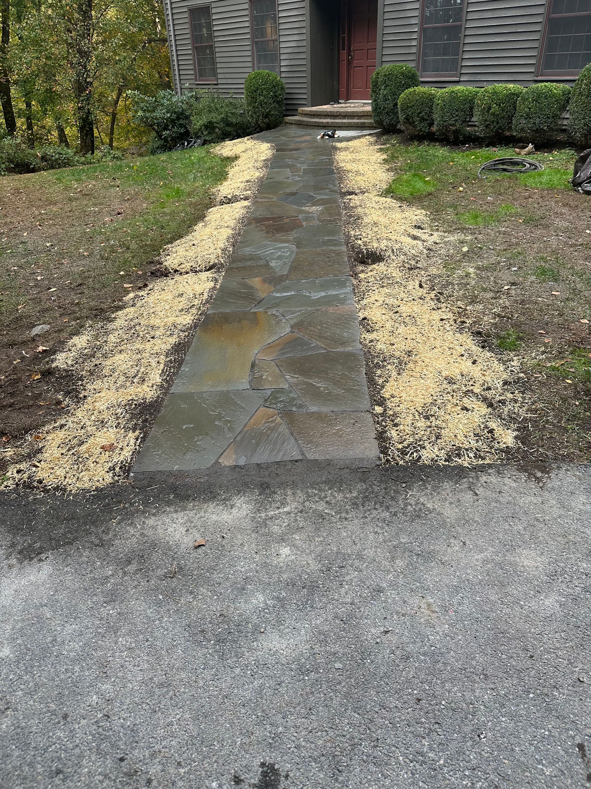 A stone pathway with wood chips on either side leads to a building with a dark door.