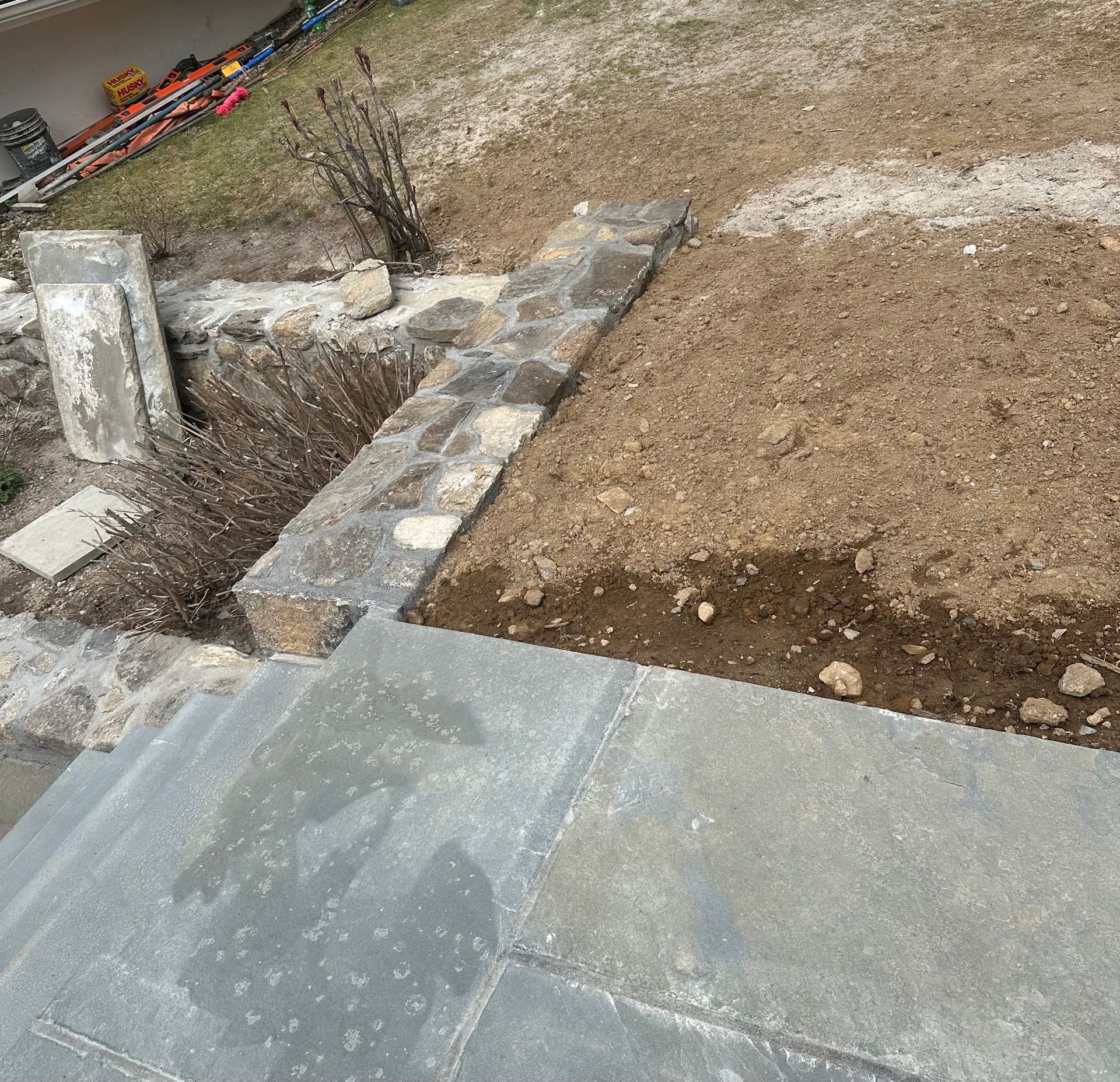 Stone steps leading to a raised garden bed with a stone border; construction debris visible.