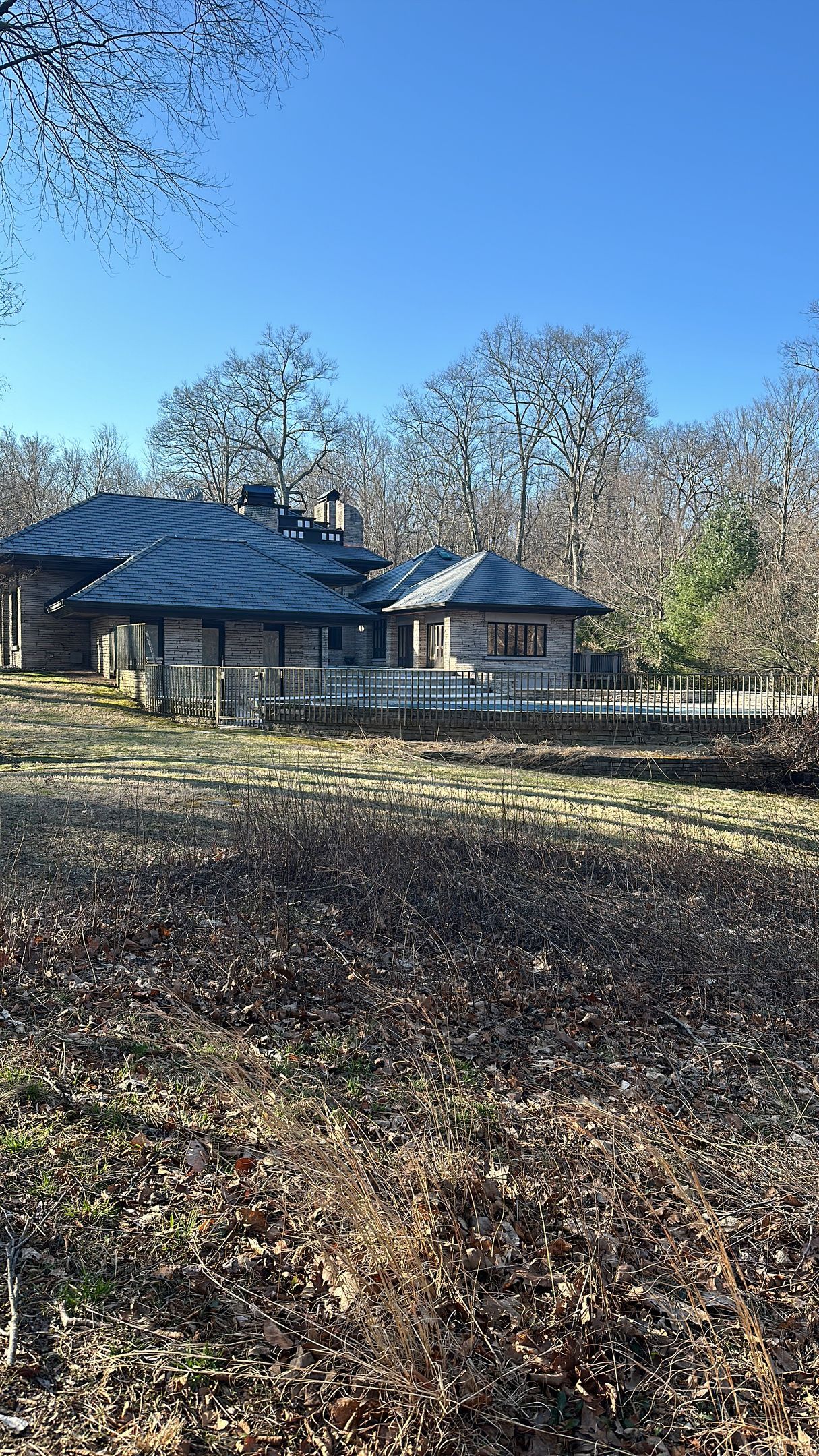 Rustic one-story building with dark roof in a wooded area under a clear blue sky.