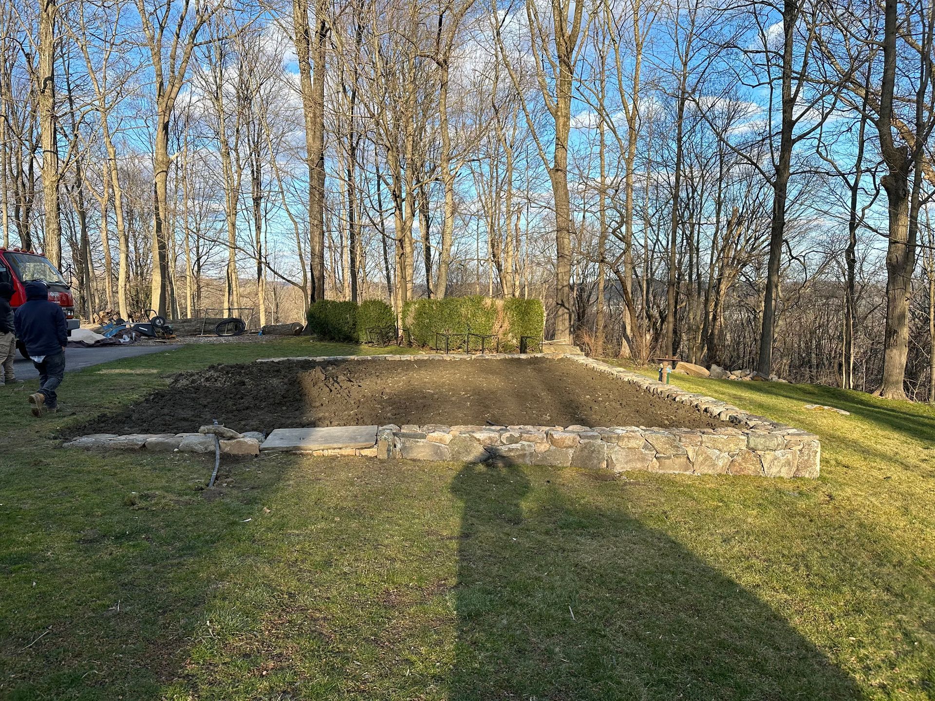 A rectangular garden bed outlined by stone borders, surrounded by grass and trees in sunlight.