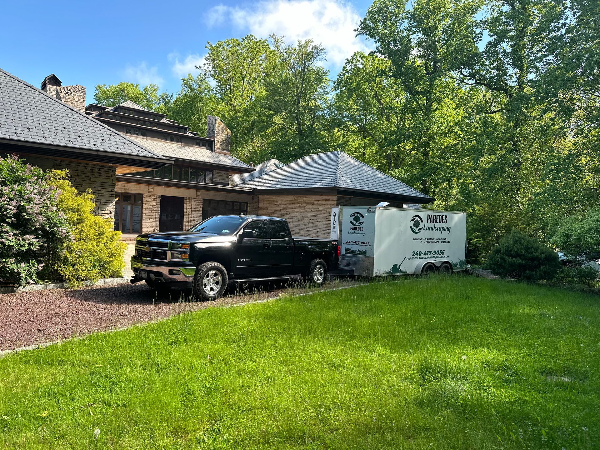 Black pickup truck and trailer parked in front of a stone building with green lawn and trees.