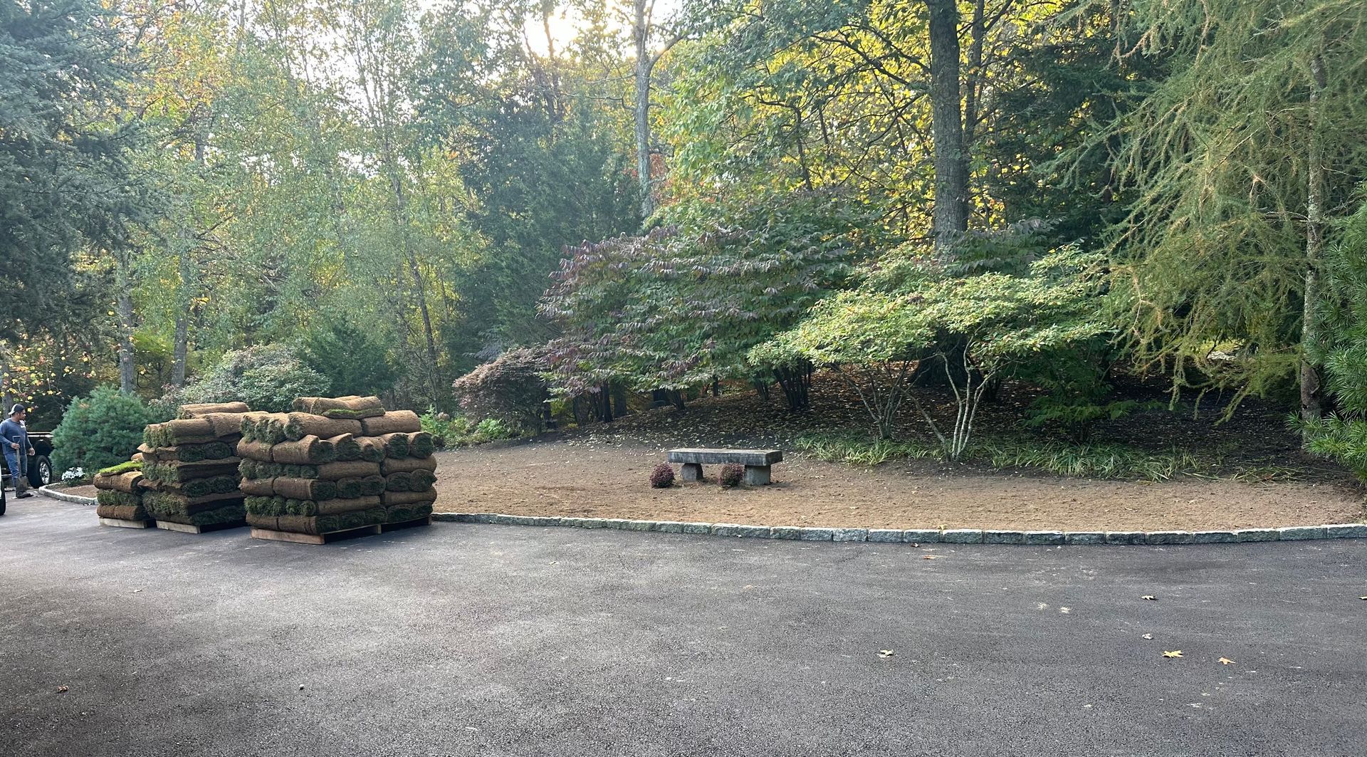 Stacks of turf on asphalt, near gravel area and trees.