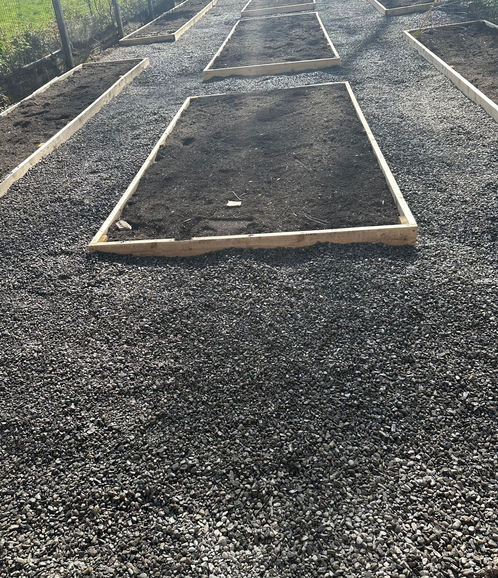 Raised garden beds filled with dark soil, surrounded by gravel.