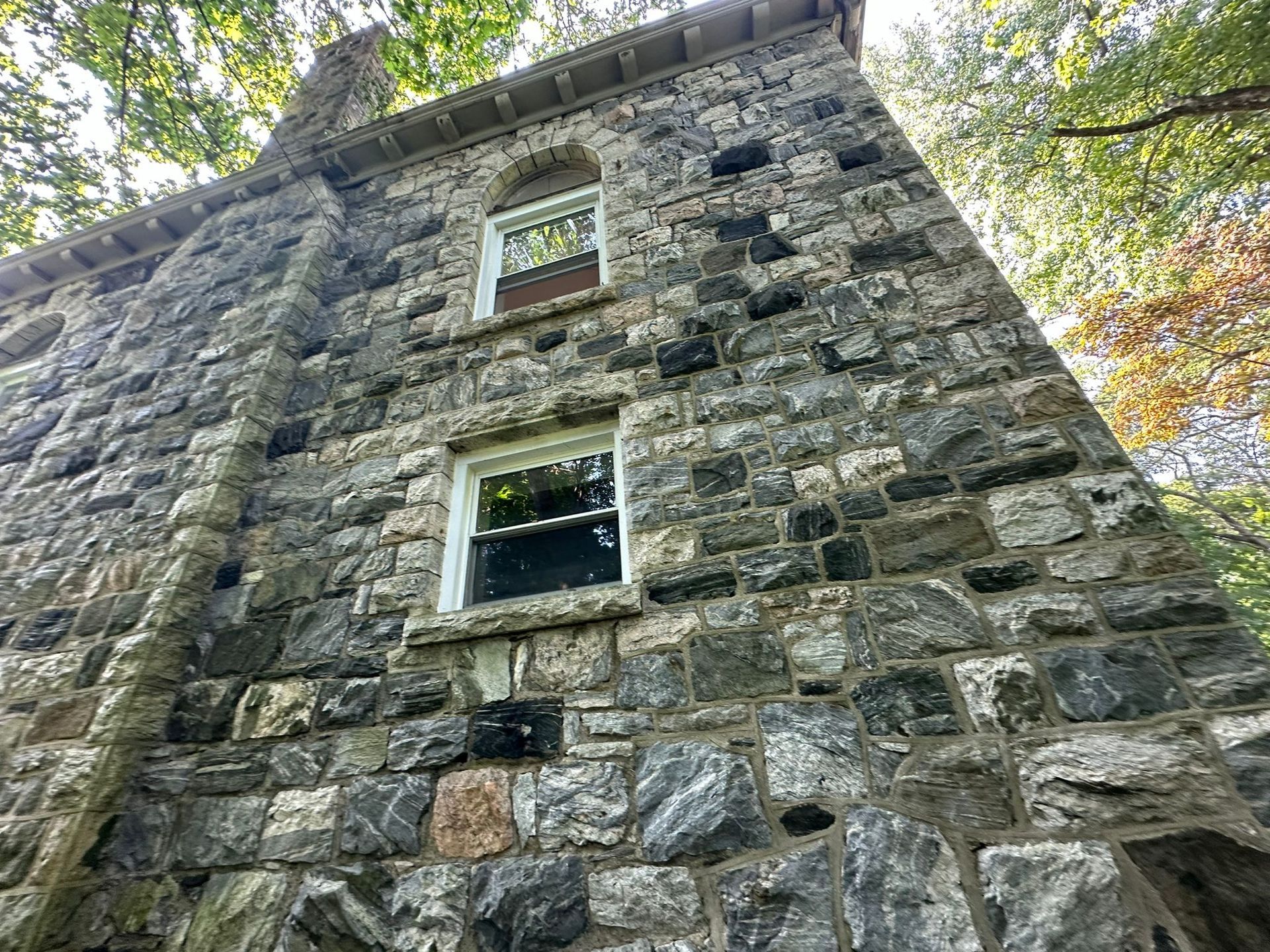 Stone tower with two white-framed windows, viewed from below, trees in background.