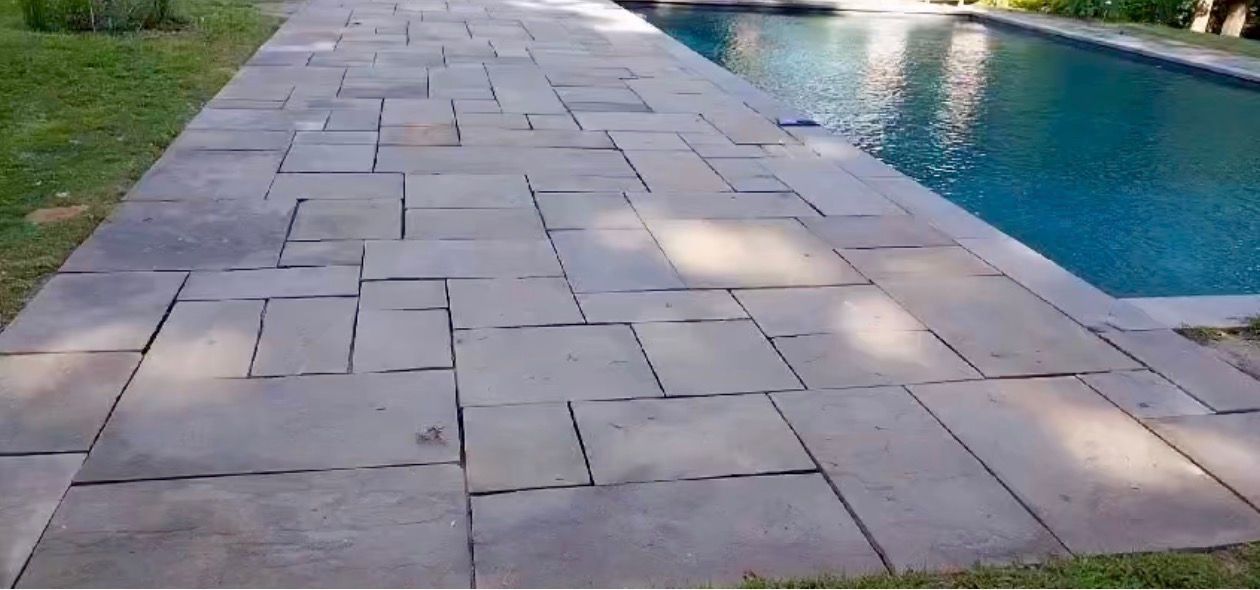 Stone walkway beside a rectangular swimming pool, with green grass on both sides.