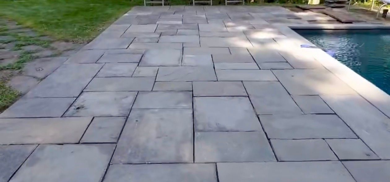 Stone patio surrounding a swimming pool with green grass in the background.