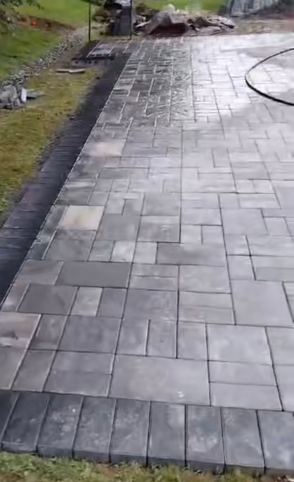 Newly installed gray brick patio with dark border, wet from washing. Outdoors, daylight.