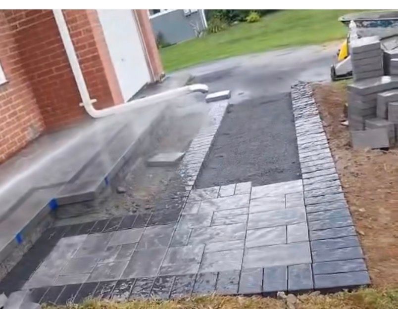 Brick patio under construction, dark grey pavers laid around steps leading to a brick building.