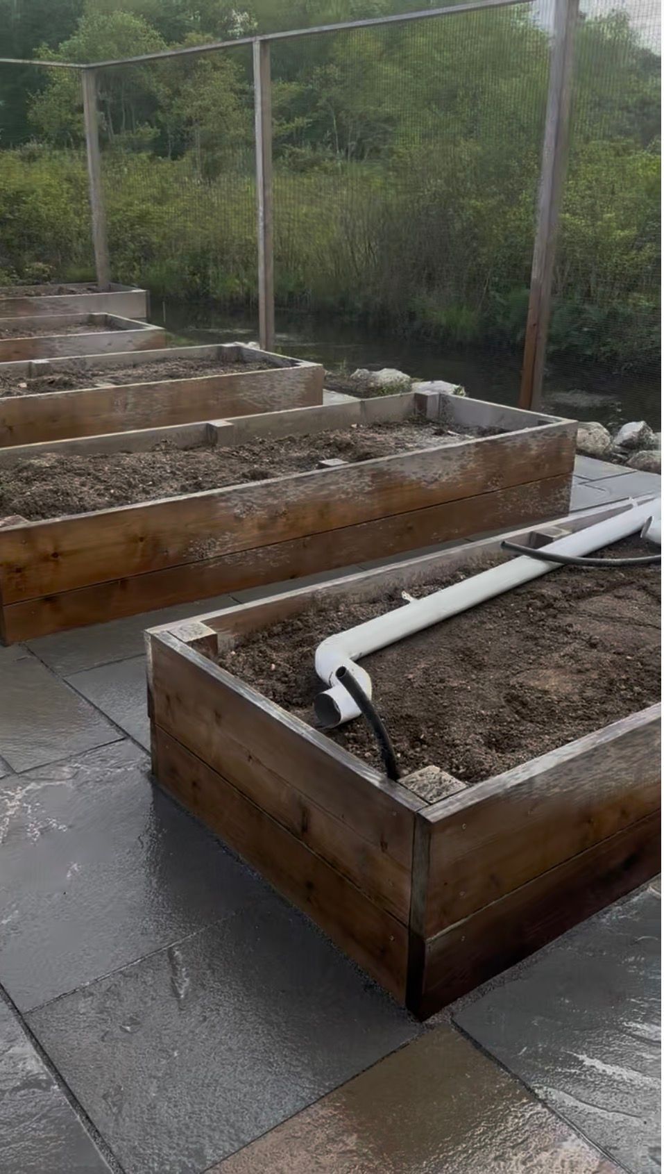 Raised wooden garden beds filled with soil, on a patio, with irrigation system installed.