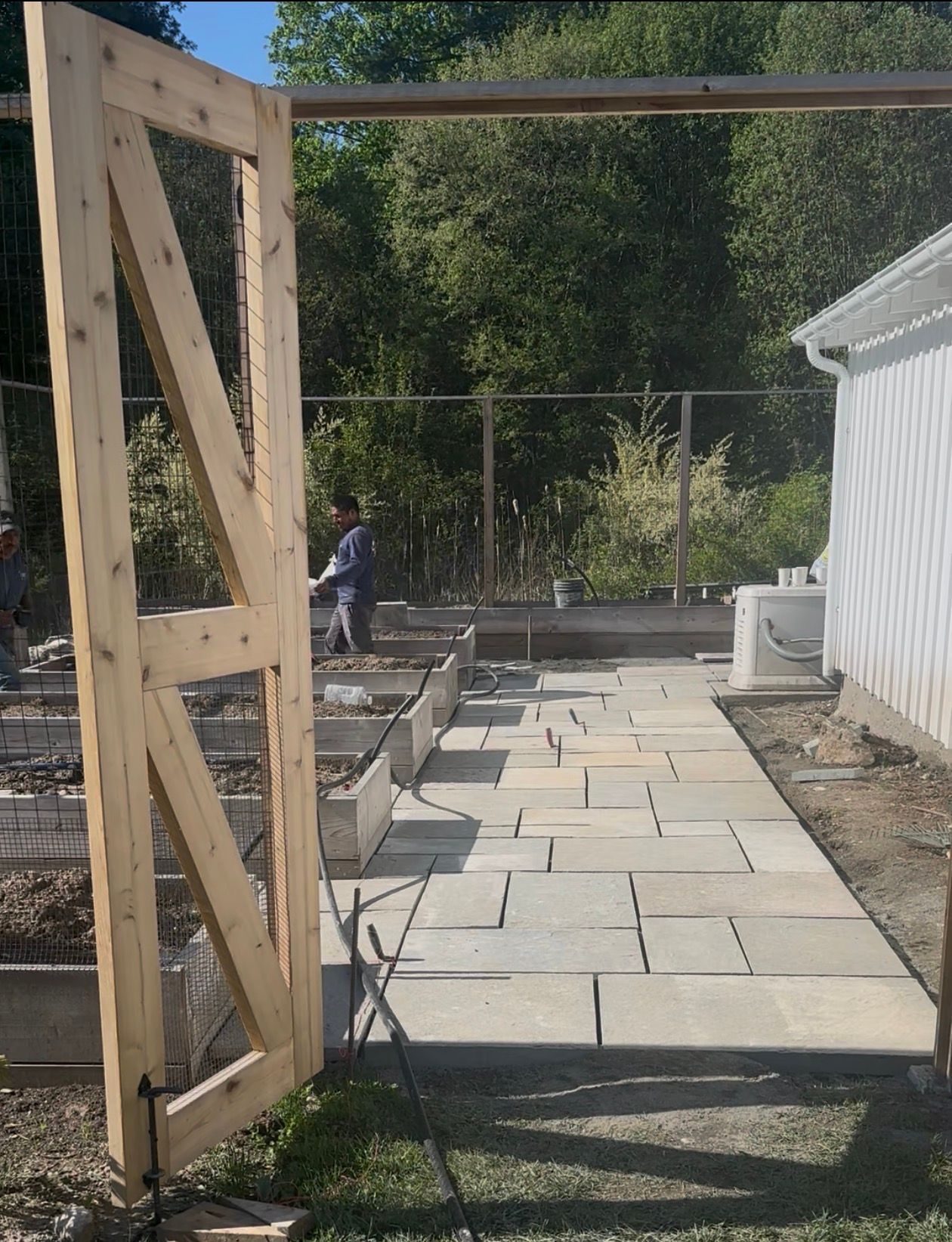 Wooden gate opens to a paved pathway beside a white building. Construction in the background.