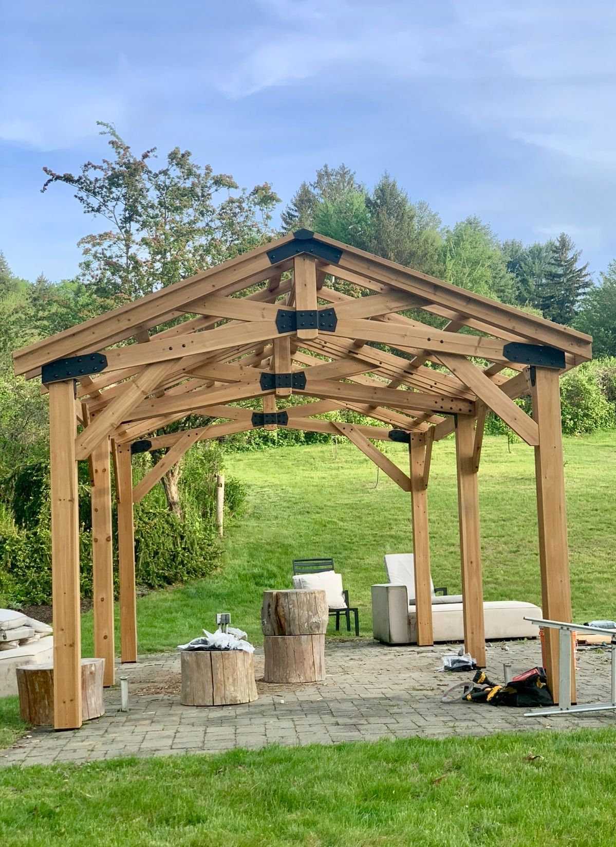 Wooden gazebo frame with a partially completed roof on a stone patio.