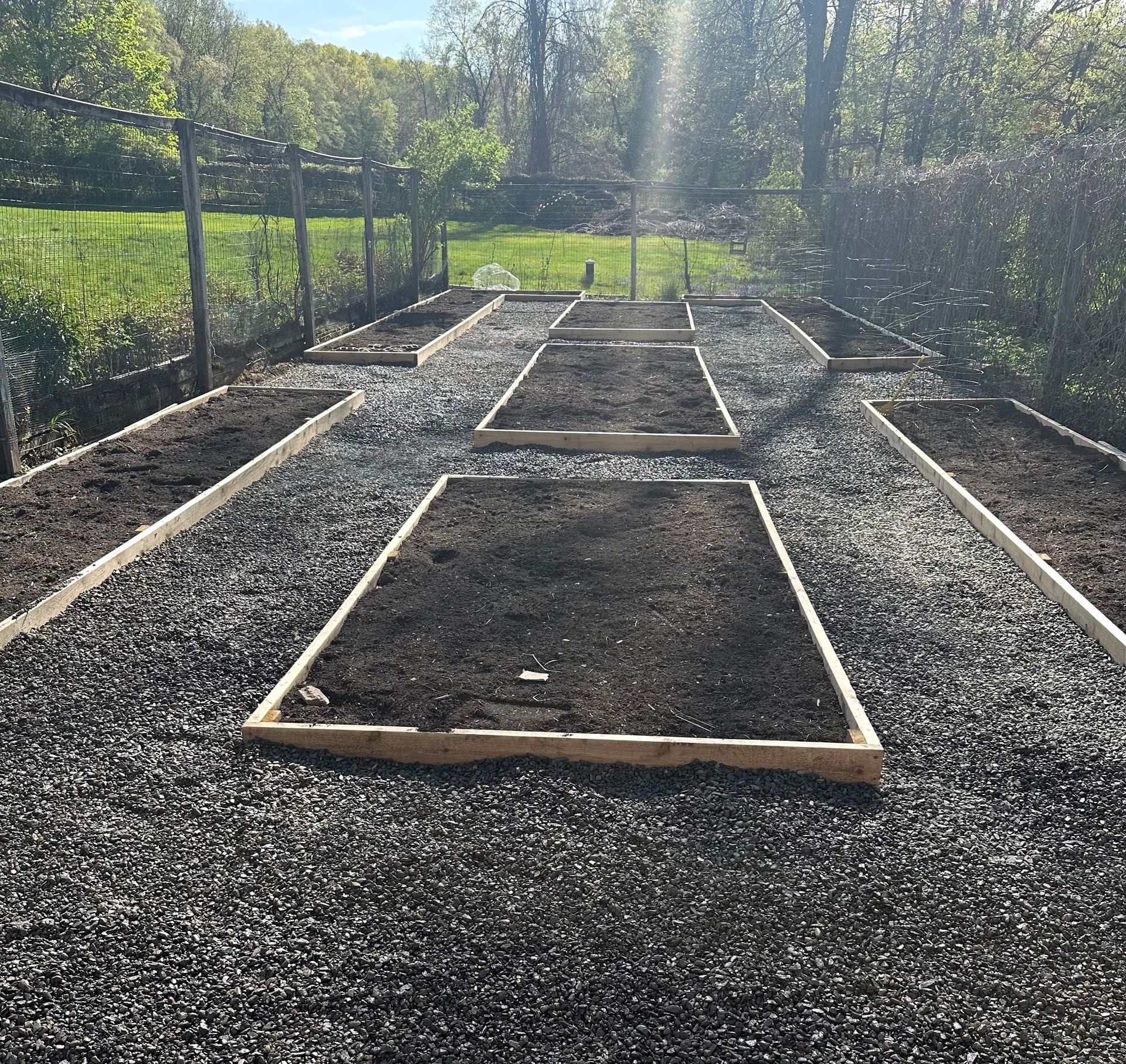 Raised garden beds surrounded by gravel in a backyard setting.