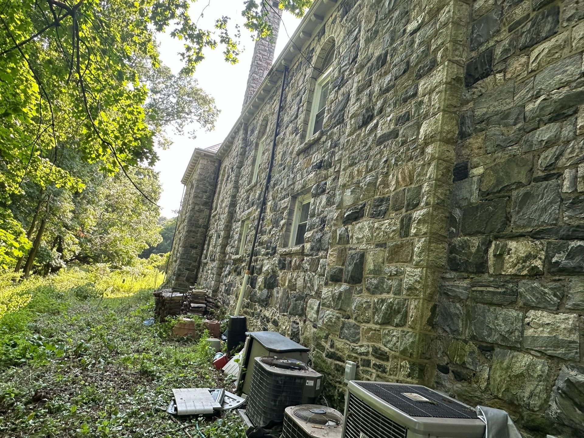 Stone wall of a building with air conditioning units and overgrown vegetation in an outdoor setting.