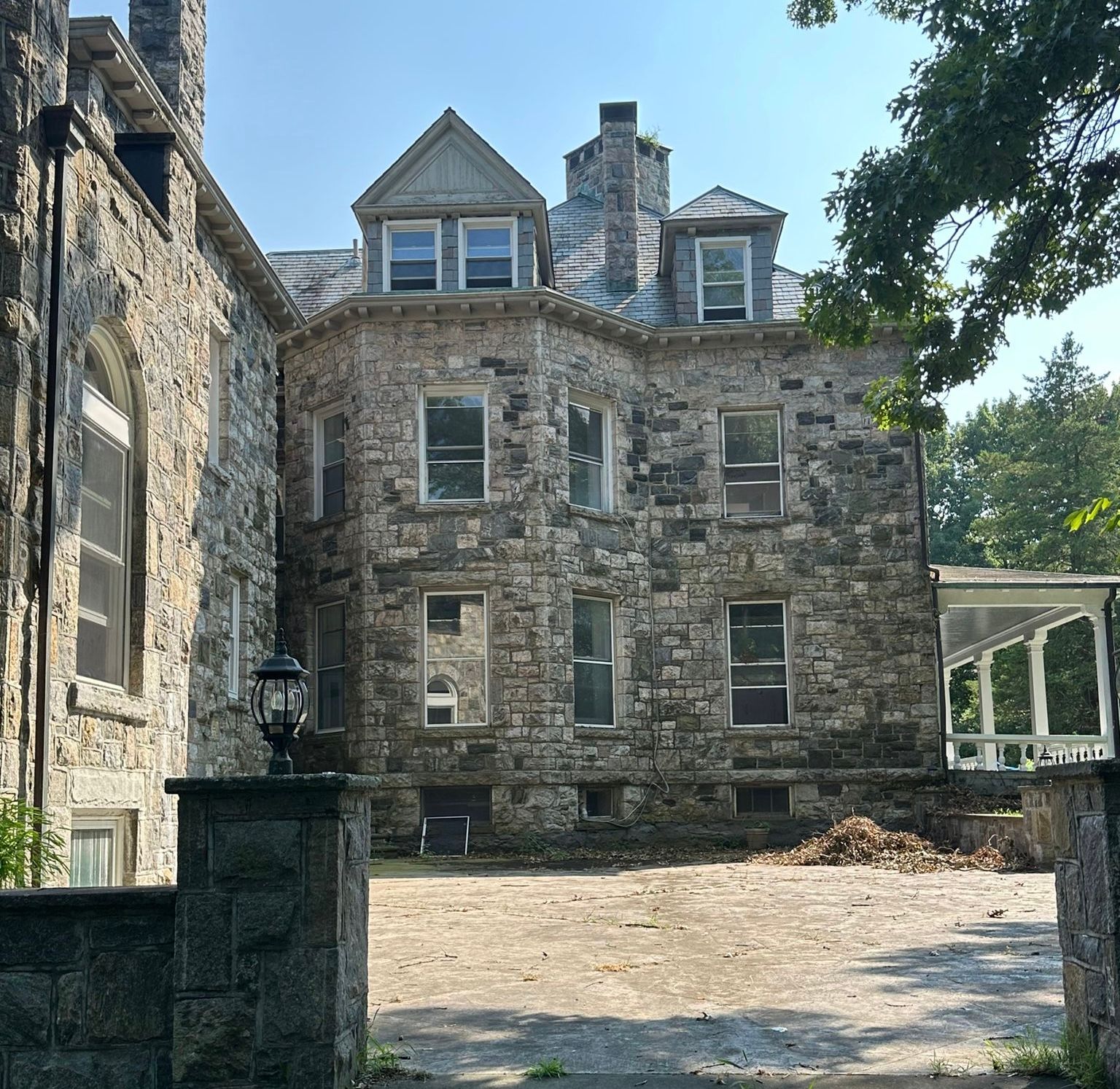 Stone mansion with multiple stories, windows, and slate roof.  A lantern sits on a stone post in the foreground.