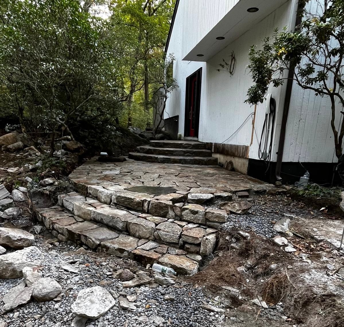Stone steps lead up to a white building's entrance, surrounded by trees and a rocky landscape.