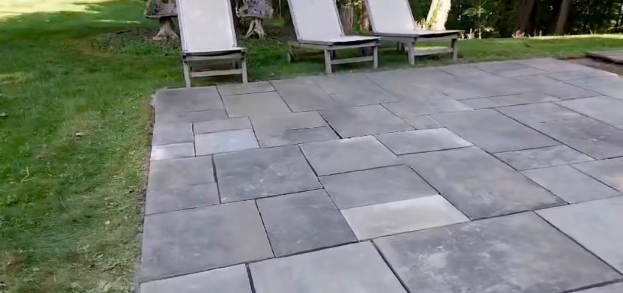 Stone patio with lounge chairs on grass.