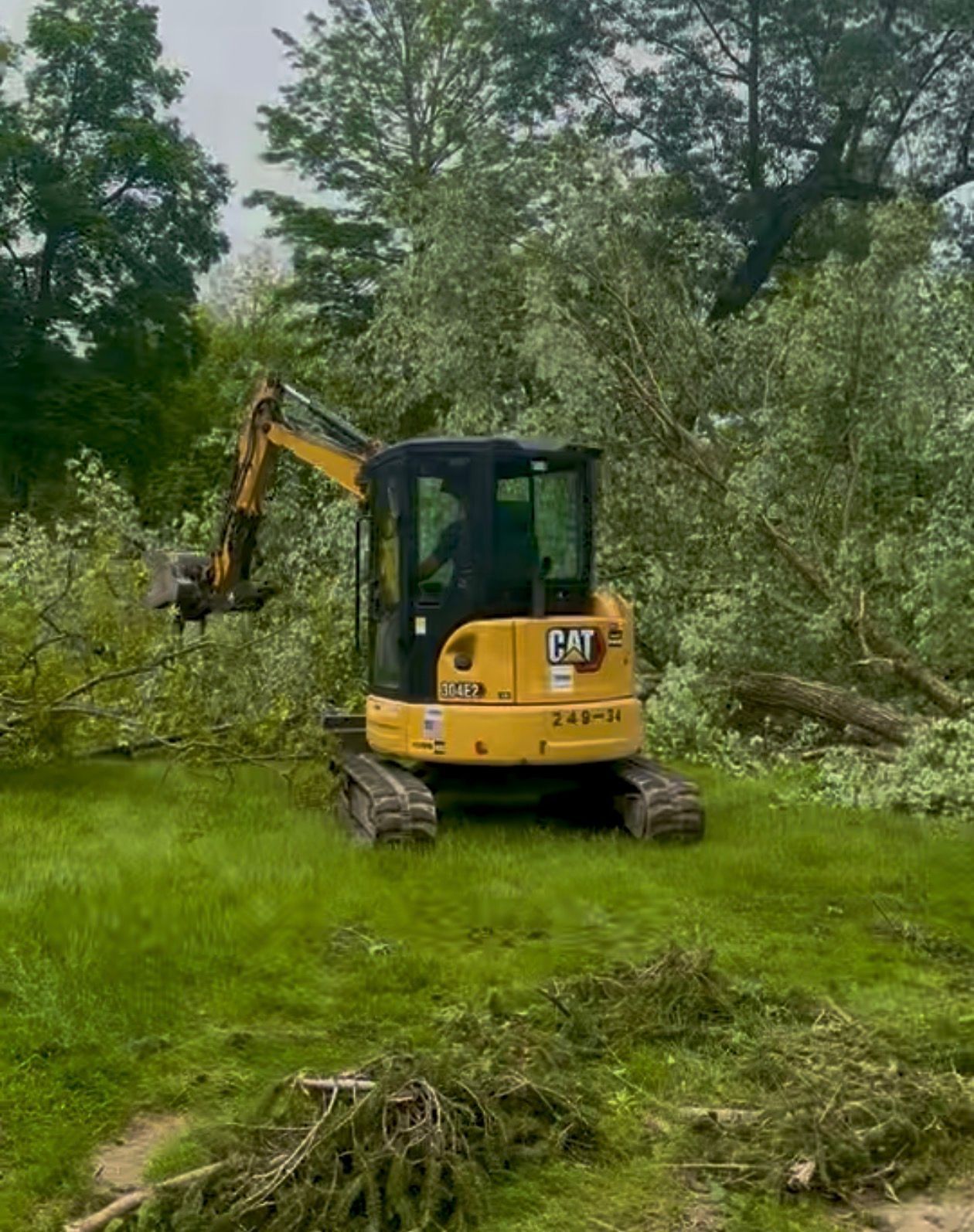 Yellow Caterpillar excavator clearing tree debris in a grassy area.
