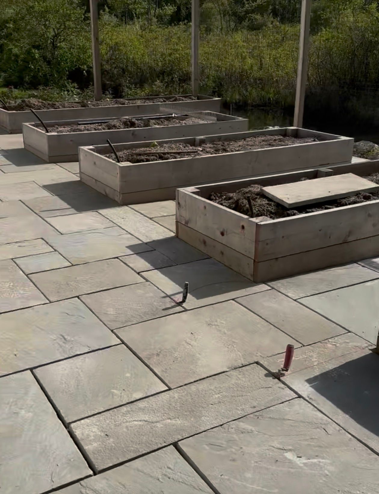Stone patio with raised garden beds; wooden frames contain soil, sunny outdoor setting.