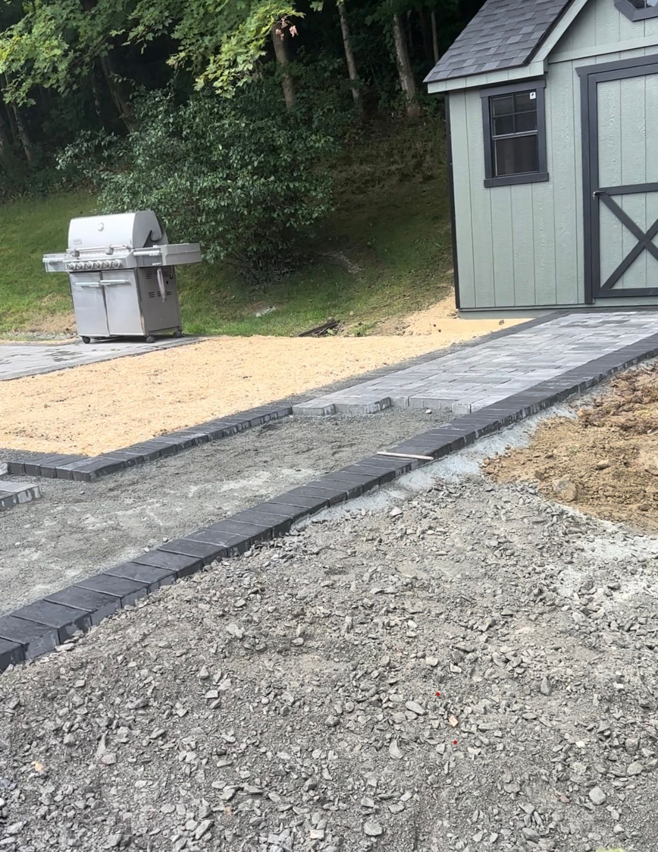 Pathway construction with gravel, pavers, and a grill near a shed.