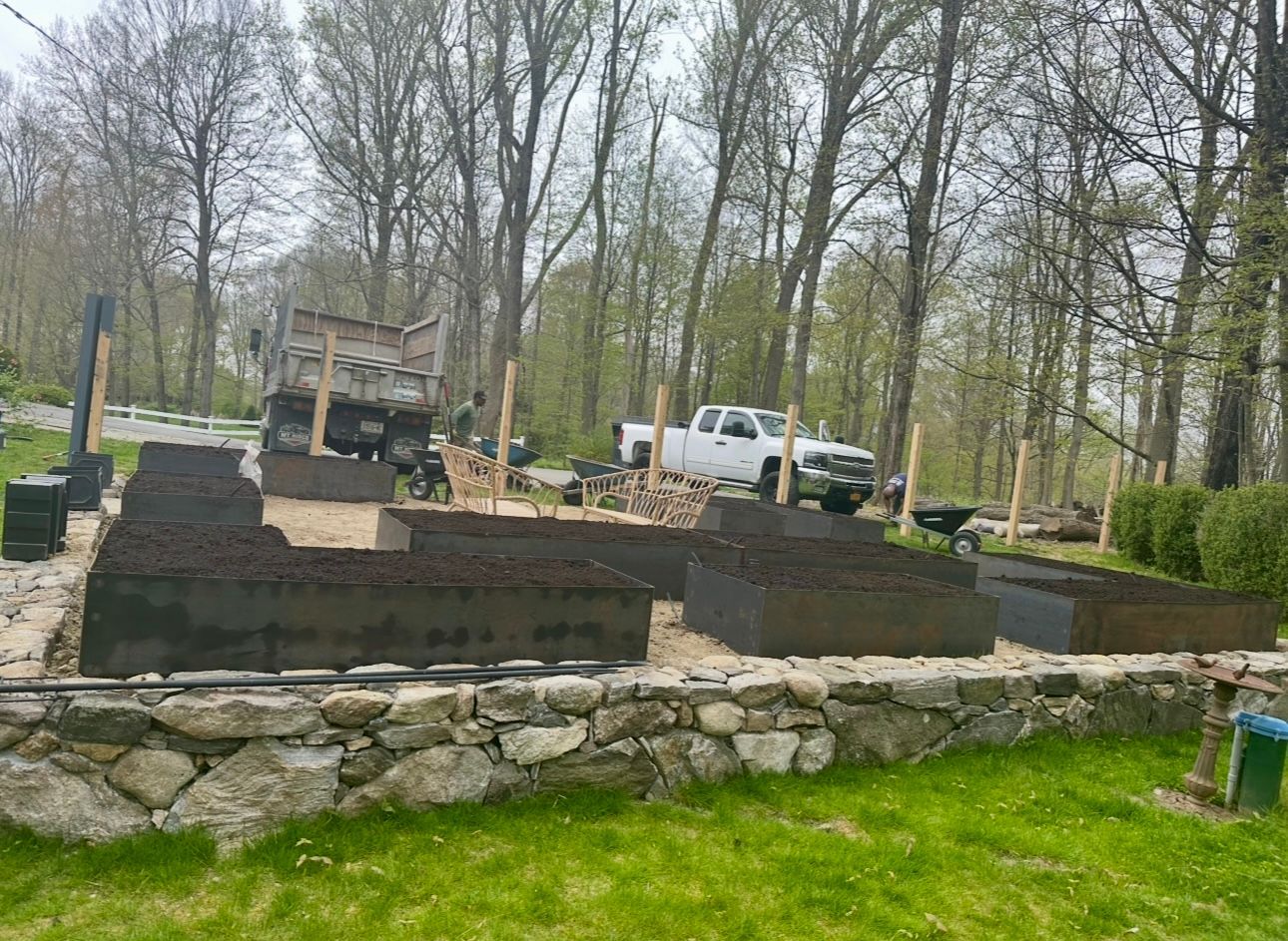 Raised garden beds filled with soil, being built on a stone wall, truck in background.