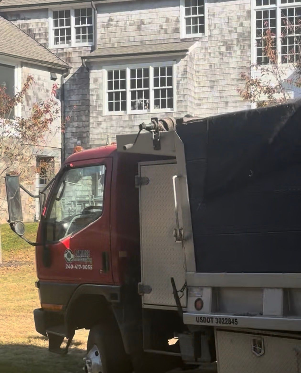 Red dump truck parked in front of a gray, shingled building with white-framed windows.