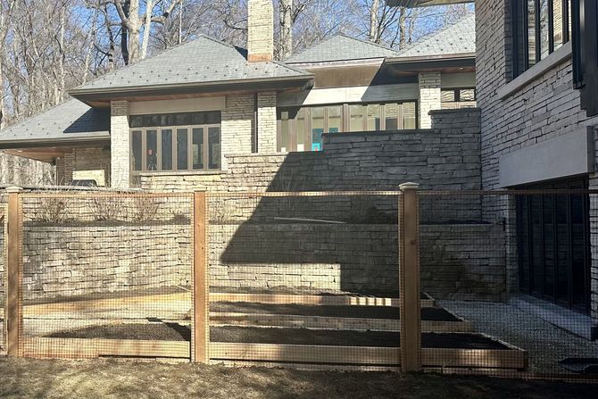 Stone house with tiered landscaping and a wooden fence.