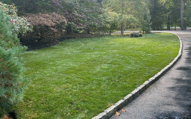 A gray two-story house with a manicured lawn, person mowing lawn.