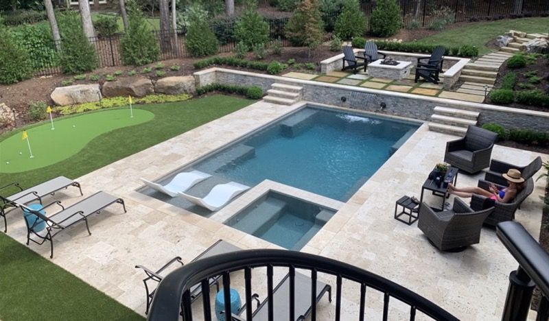 A large swimming pool is surrounded by a stone patio and a wooden fence.