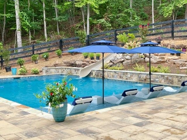 A large swimming pool with a hot tub in the middle is surrounded by trees.