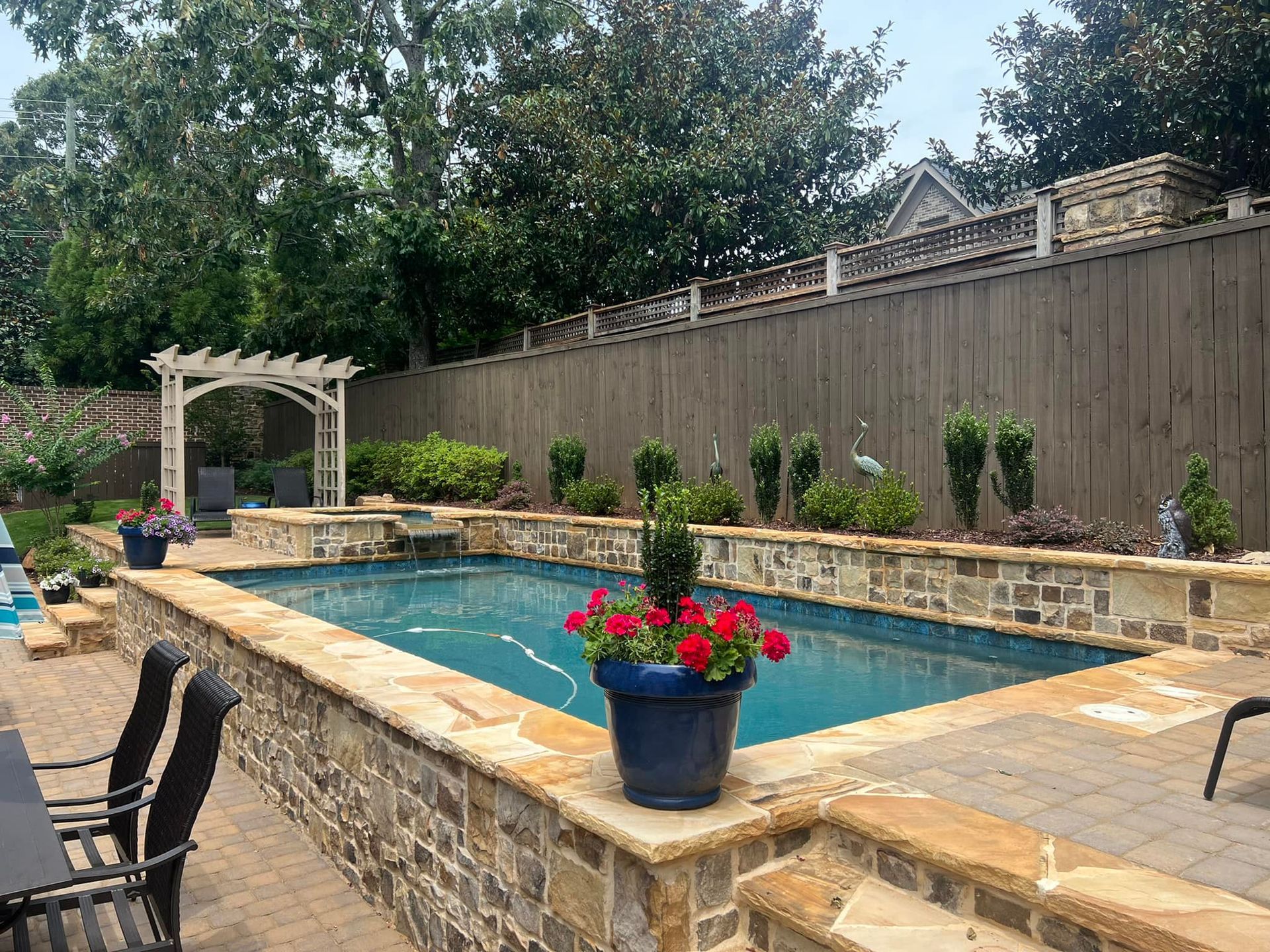 A large swimming pool is surrounded by a stone wall and chairs.