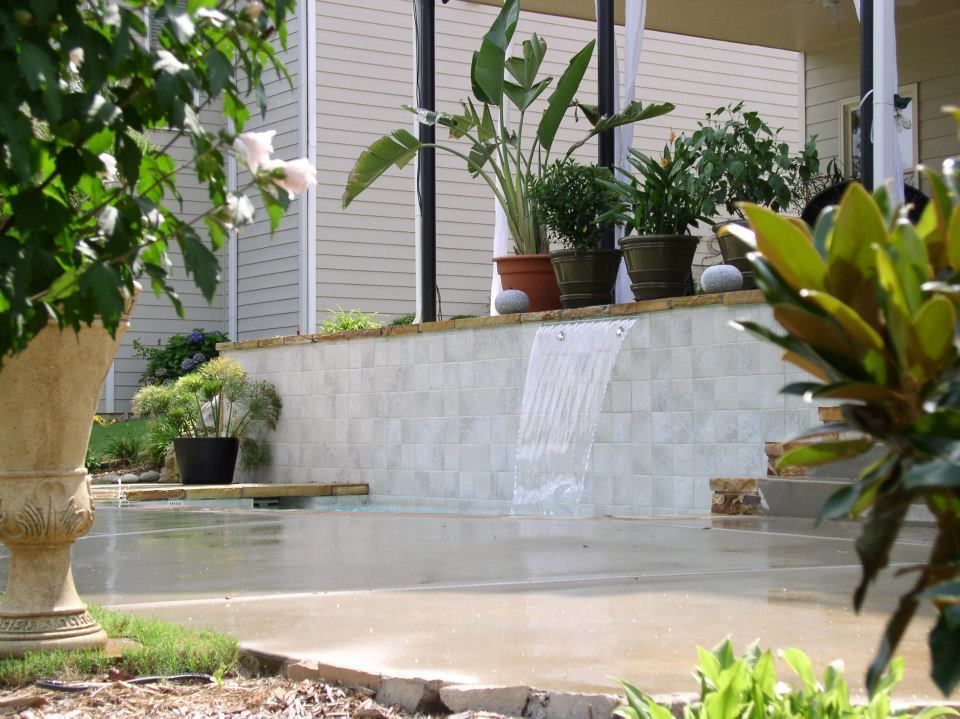A waterfall is surrounded by potted plants in front of a house
