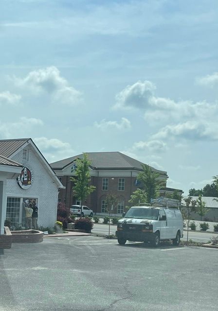 White van in a parking lot in front of a building with a brick building in the background under a cloudy blue sky.