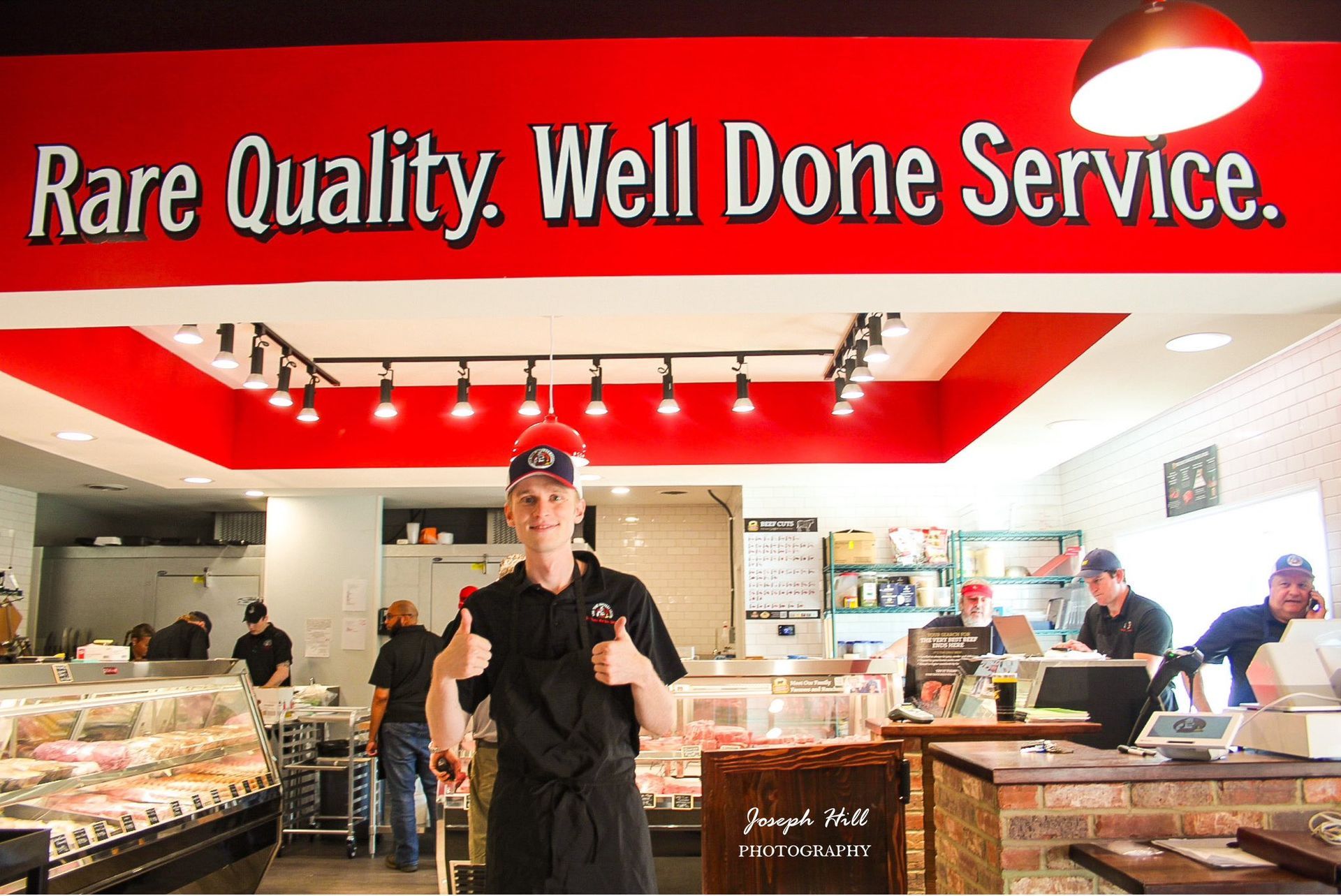 Butcher shop interior: smiling employee gives thumbs up under sign 