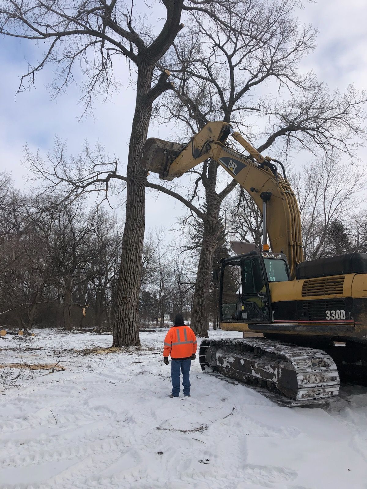 A man is standing in the snow next to a large excavator