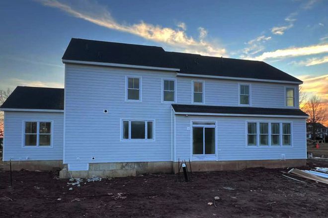 New white two-story house under construction with a dark roof and an unfinished dirt yard