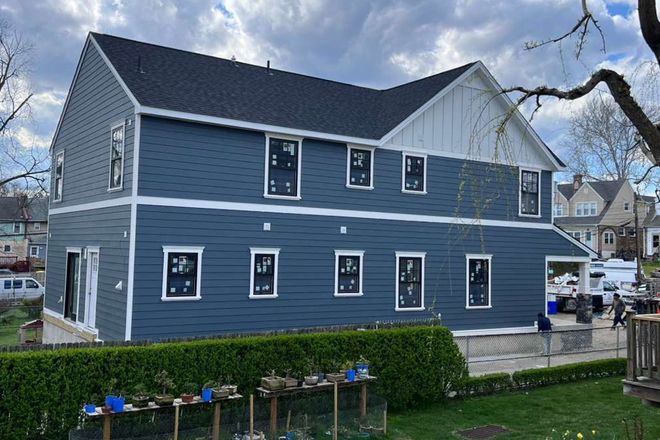 Blue two-story house with white trim and a dark roof, viewed from the yard on a cloudy day