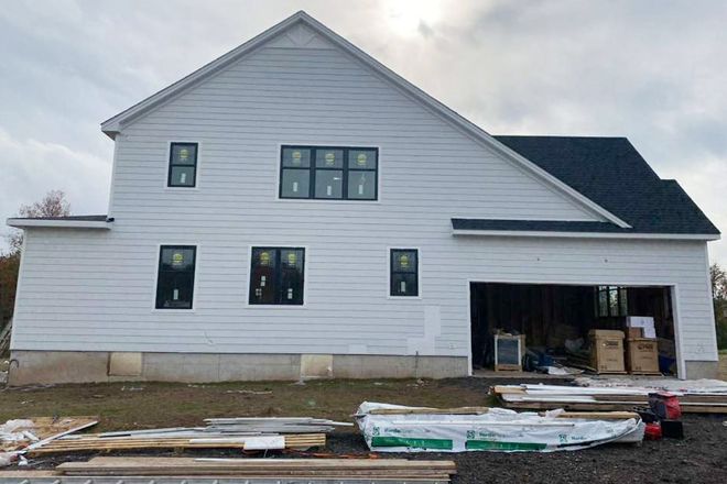 A partially built white two-story house with dark roof and open garage in a muddy construction site