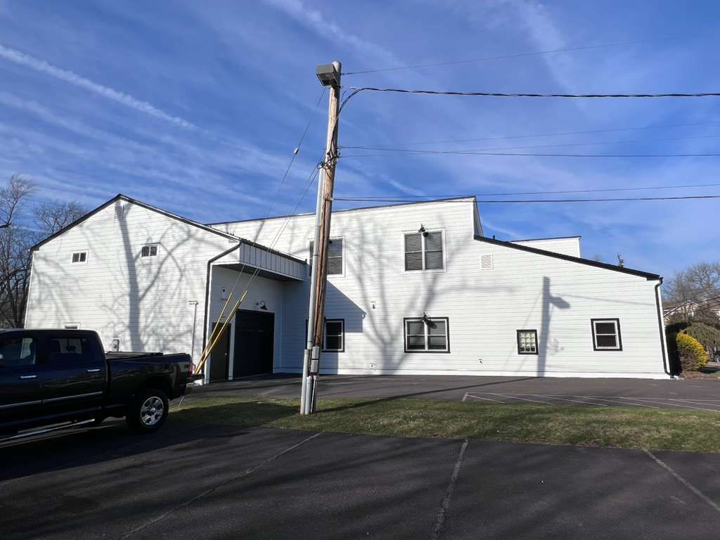 A white, two-story commercial building with black trim, seen from a parking lot on a sunny day with a utility pole in front.