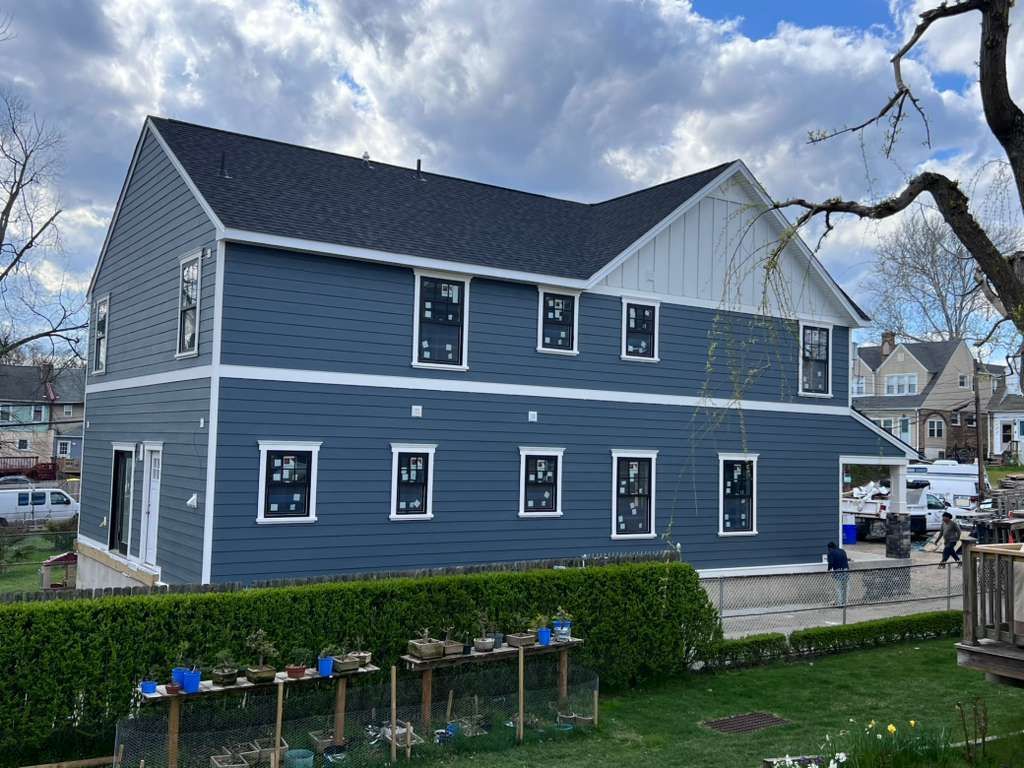 A blue, multi-story house under construction with white trim, dark roof shingles, and installed window frames.
