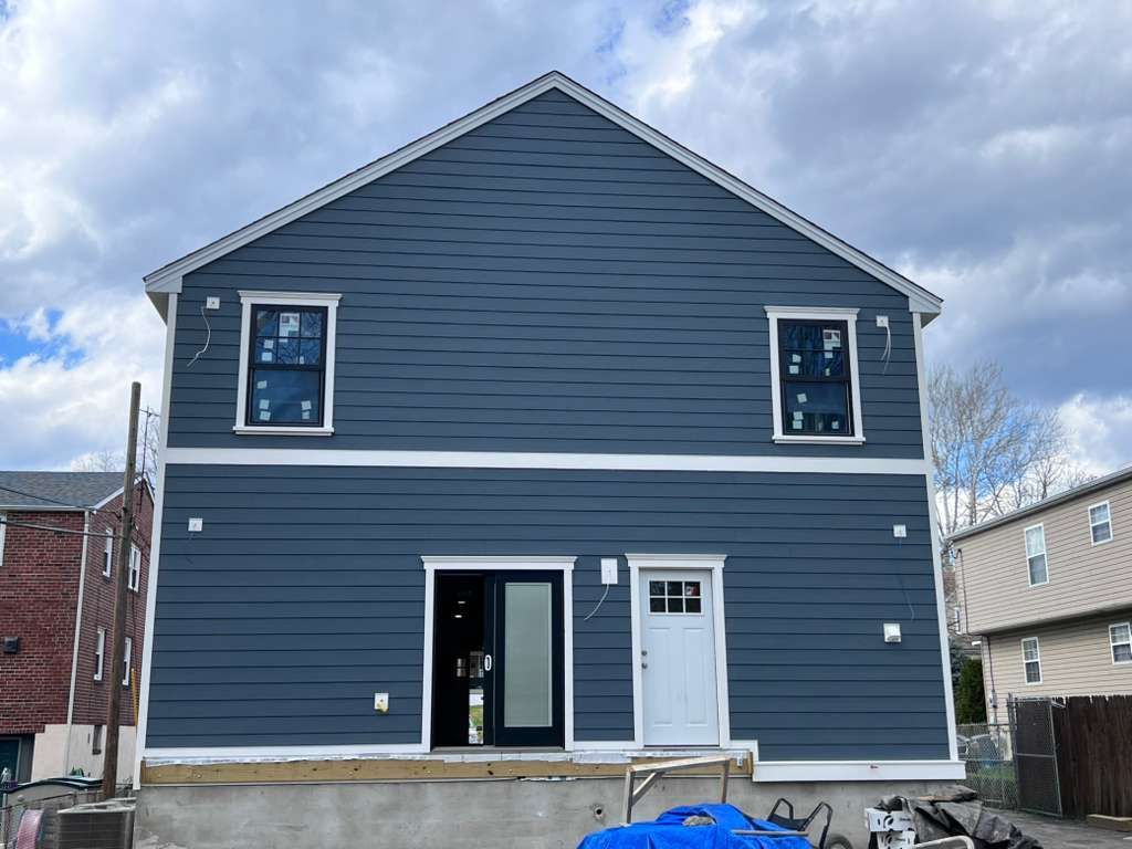 A blue, two-story house under construction with white trim, two upper windows, a sliding door, and a white entry door.