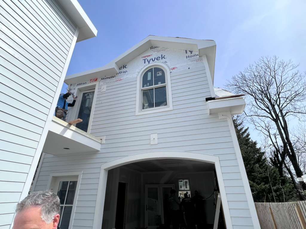 A construction worker stands on a balcony during the siding installation of a two-story house with a partially open garage.