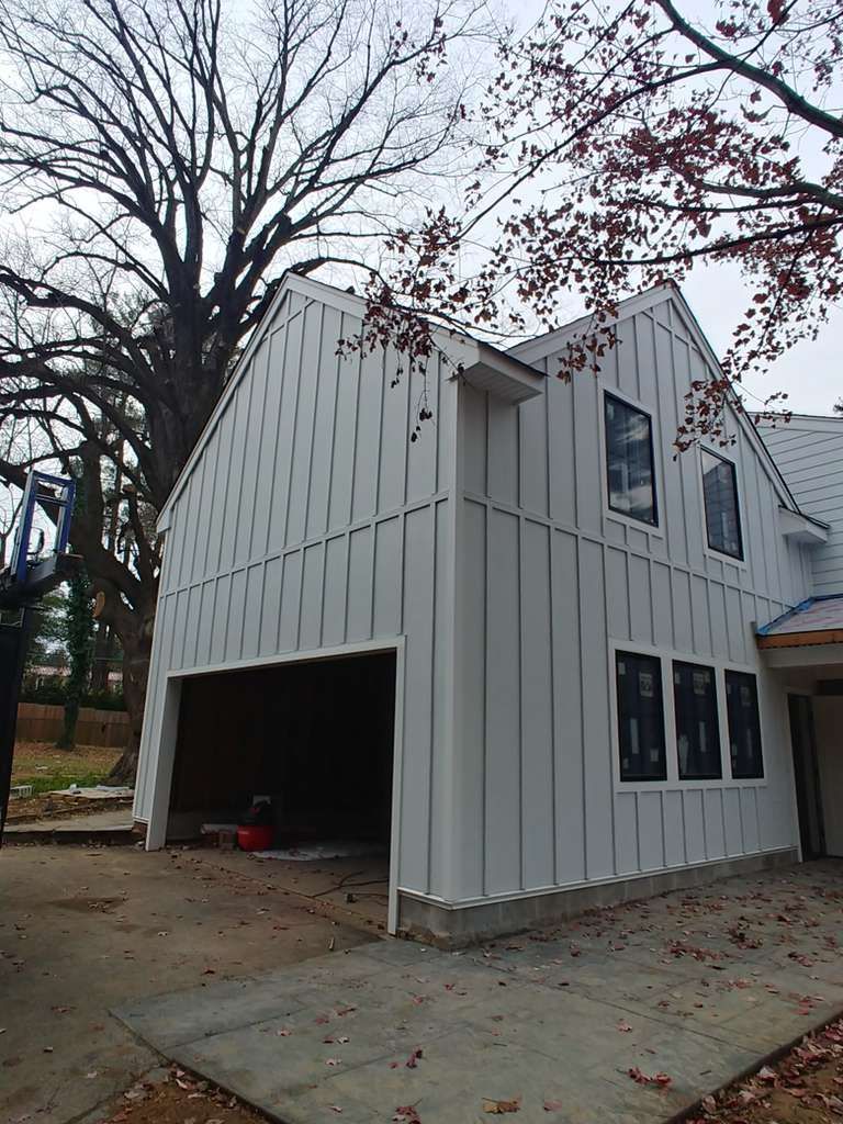 A side view of a house addition under construction with white board-and-batten siding and black window frames.
