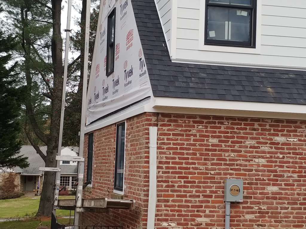 A partially renovated two-story home featuring a lower brick exterior and upper level with white siding and a dormer.