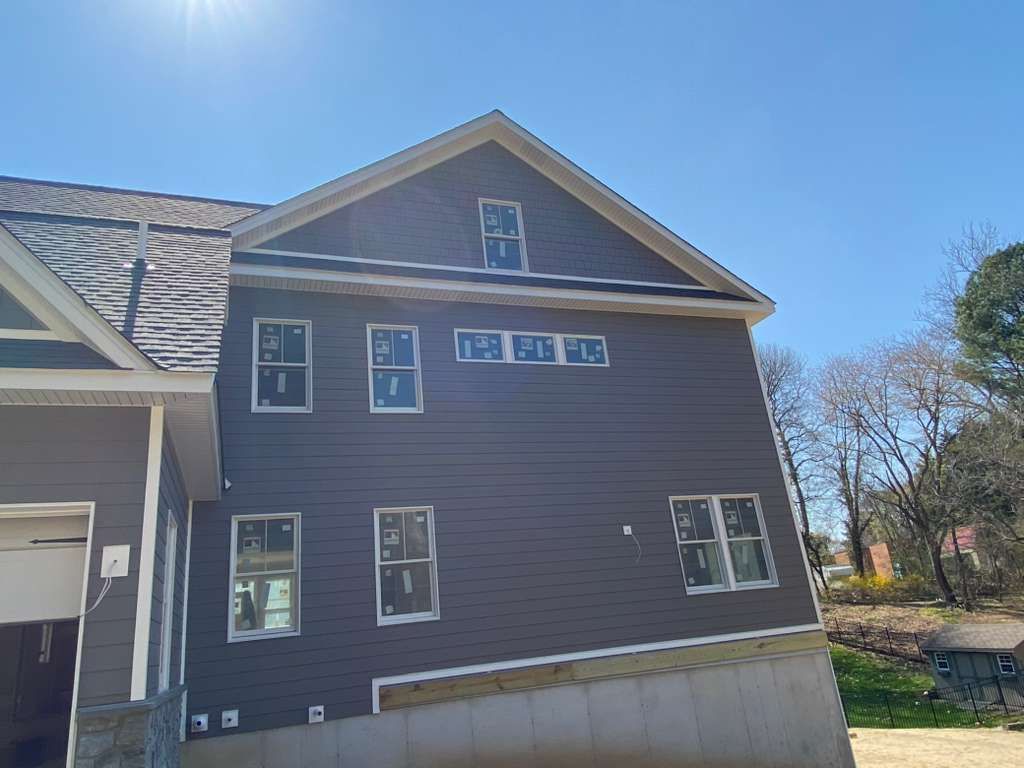 Side view of a dark gray house under construction with a concrete foundation, covered windows, and a clear blue sky.