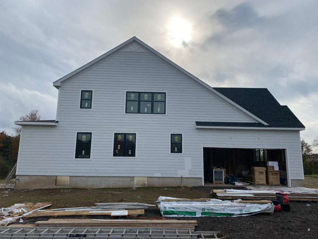 A side view of a newly constructed white, two-story house with black-framed windows and an open garage under a cloudy sky.