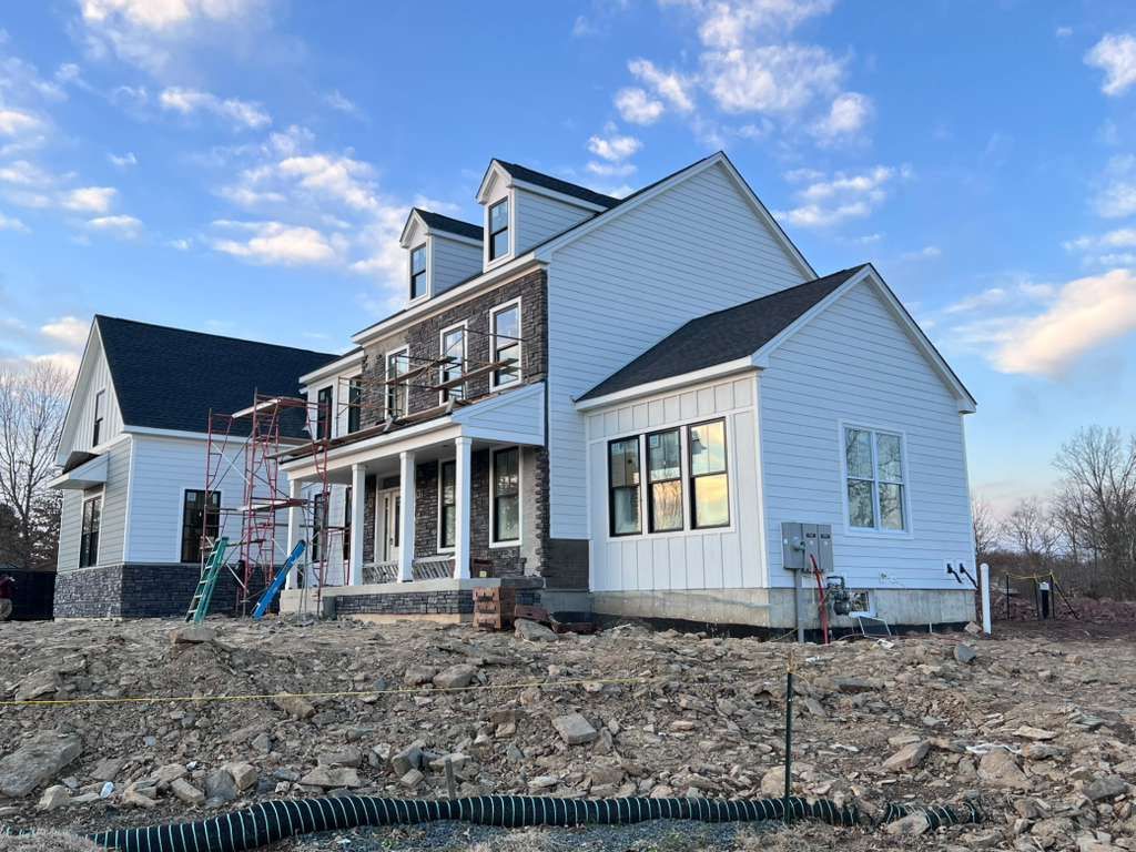 A new two-story suburban home under construction with white siding, stone accents, a dark roof, and scaffolding.