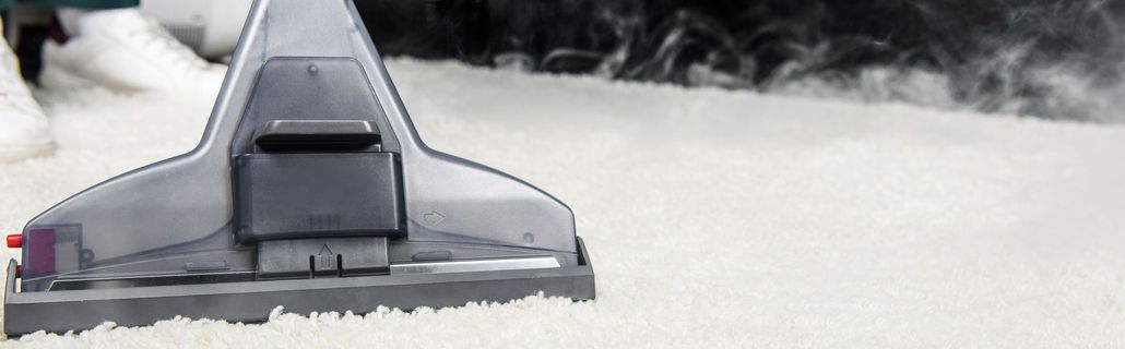 A vacuum cleaner is cleaning a white carpet, producing steam.