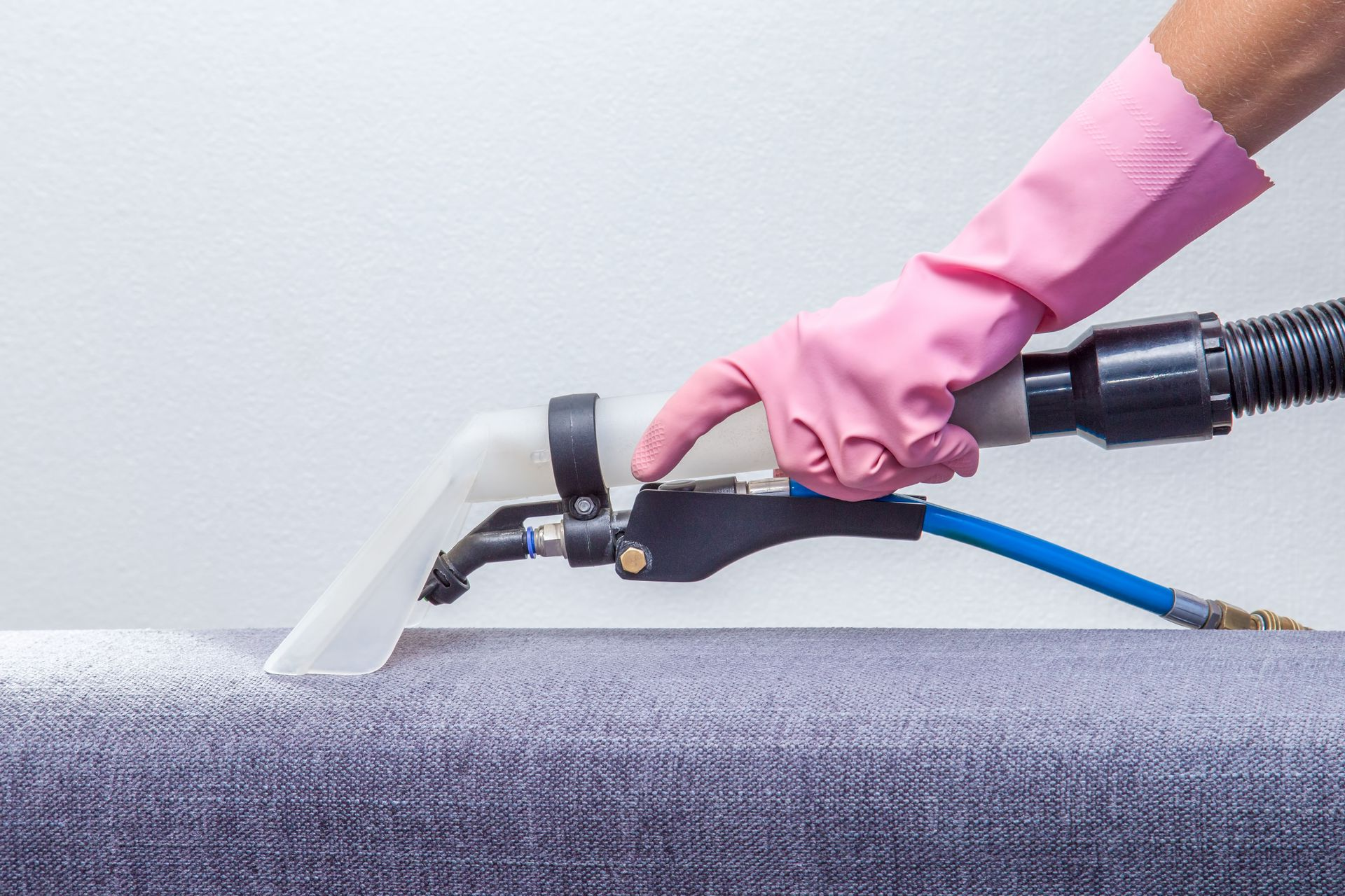 Person in pink glove using upholstery cleaner on gray fabric.