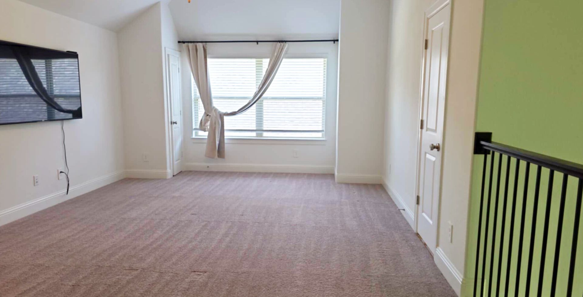 Empty room with carpet, window, TV, door, and railing.