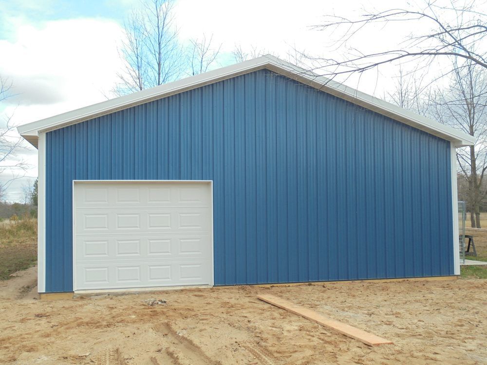 A blue garage with a white garage door is sitting on top of a dirt field.
